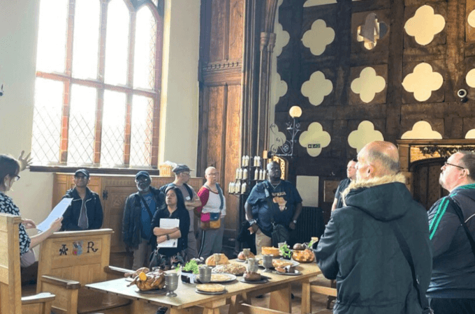 Manchester Deaf Centre – A group of people are gathered around a banqueting table in a great Tudor Hall. A man is on the left of the photo is signing.