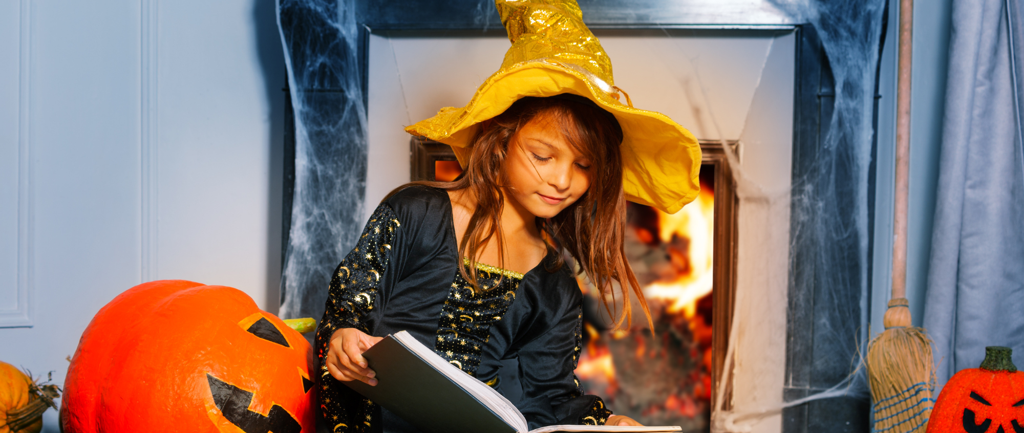 Young girl in a witches hat and book sat on a bed
