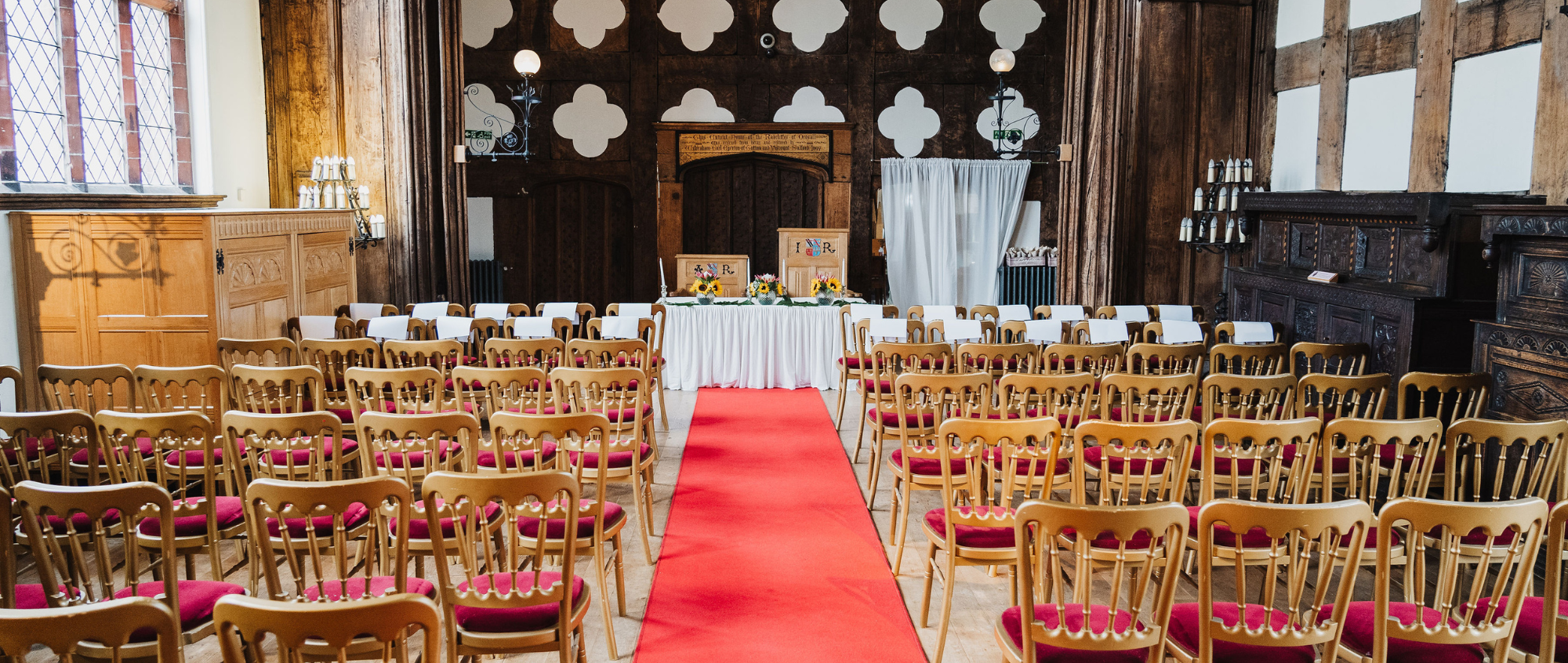 Wedding set up in the Great Hall with brown wooden chairs and a red carpet