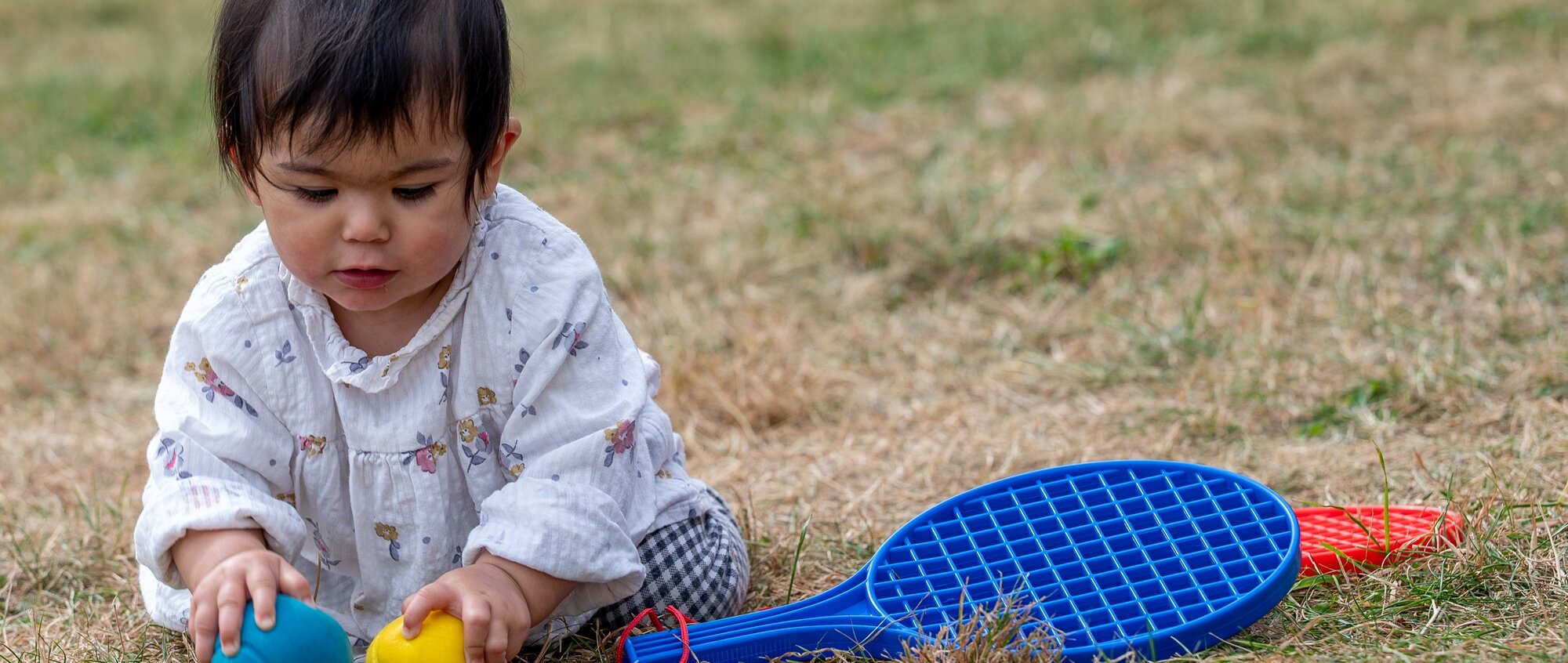 A toddler plays with bats and balls on the lawn.